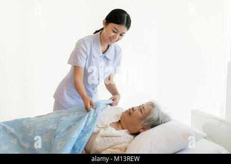Asiatische Krankenschwester in der Altenpflege decken Sie mit einer Decke für ältere Menschen im Pflegeheim. Stockfoto