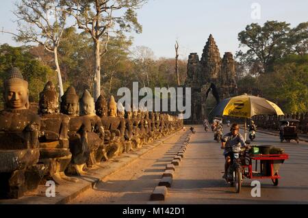 Kambodscha, Angkor, als Weltkulturerbe von der UNESCO, Traveling salesman auf Motorrad vor eine Reihe von Bodhisattava Statuen am Eingang des Bayon, die wichtigsten Tempel der alten Khmer Stadt Angkor Thom Stockfoto