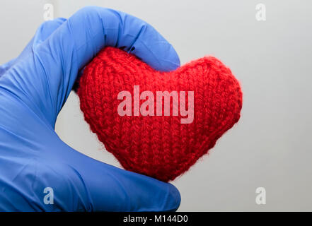 Warmen gestrickten roten Herzen Halten einer Hand in medizinische Handschuhe Stockfoto