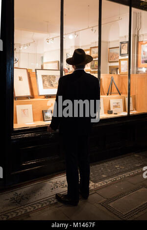 Ein Mann mit Hut steht an Gemälde im Fenster einer Kunst Galerie suchen, am 15. Januar 2018 in London, England. Stockfoto