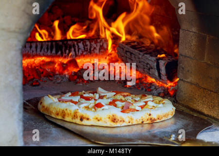 Close up Pizza im Holzofen mit Flammen hinter Stockfoto