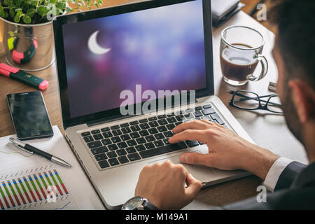 Mann bei der Arbeit im Büro. Halbmond auf blauen Himmel Hintergrund auf dem Bildschirm. Stockfoto