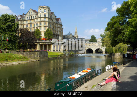 Bath, Großbritannien - 3.. Juli 2011: Frauen sitzen in der Sommersonne neben den bunten Kanalbooten, die auf dem Fluss Avon in der Nähe des Stadtzentrums von Bath, Somerset, Großbritannien, festgemacht sind. Bath ist ein UNESCO-Weltkulturerbe und berühmt für seine Architektur. Stockfoto