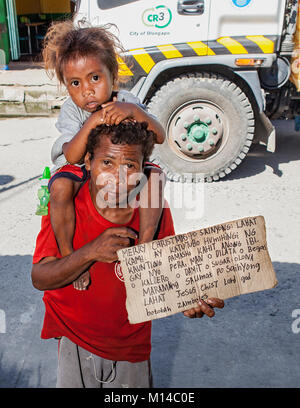 Ein Filipino Aeta Mensch sein Kind auf seine Schultern und ein Zeichen für Nahrung und Arbeit und mit einem Weihnachtswunsch in Barretto Stadt, Luzon, Philippi. Stockfoto