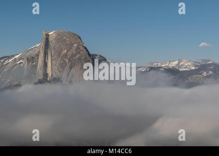 Schuss des Half Dome, über den Wolken, mit einer Wolkendecke, einige schneebedeckte Berge und einem klaren blauen Himmel, vom Glacier Point, Yosemite National Park Stockfoto