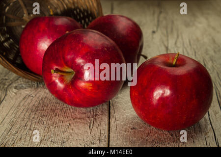 Rote Äpfel in einem Weidenkorb auf einer hölzernen Hintergrund verstreut Stockfoto