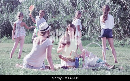 Portrait von lächelnden Mamas auf Picknick im Sommer Park mit glücklichen Kindern hinter dem Spielen Stockfoto