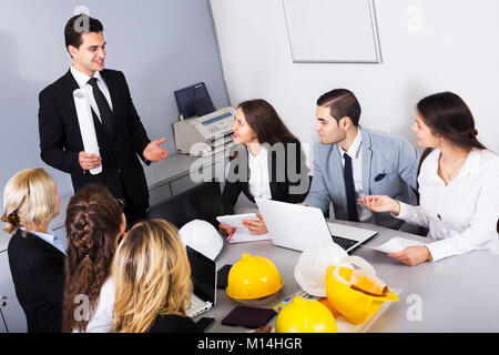Team von positiven Ingenieure Diskussion von Projekt- und lächelnd im Büro. Fokus auf Sitzen der Mensch Stockfoto