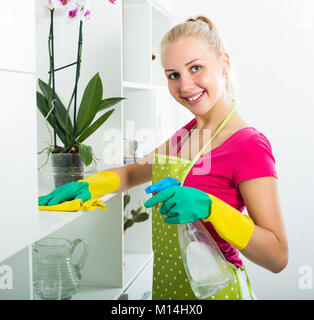 Freudige junge blonde Mädchen in der Schürze und Handschuhe Reinigung von Oberflächen zu Hause Stockfoto