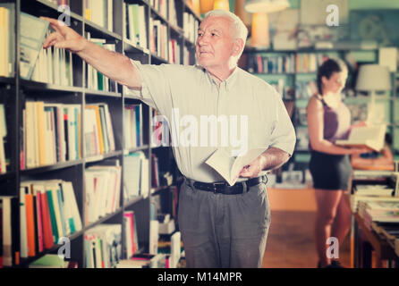 Mann 61-67 Jahre alt ist die Wahl Buch in der Buchhandlung. Stockfoto