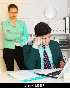 Jungen betonte Geschäftsmann im Büro mit den Unzufriedenen weiblichen Kollegen hinter Stockfoto