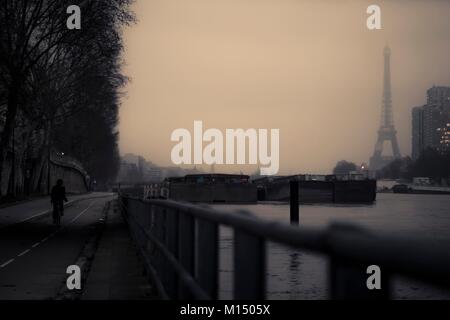 Blick auf die Seine mit einem Mann auf einem Fahrrad auf dem Bahndamm einen entfernten Eiffelturm durch Nebel oder Dunst verdeckt in Paris, Frankreich Stockfoto