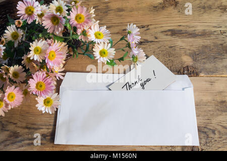 Umschlag mit einer Karte mit handschriftlichen Text - Danke mit einem Blumenstrauß aus zarten rosa Chrysanthemen auf einer hölzernen Hintergrund Stockfoto