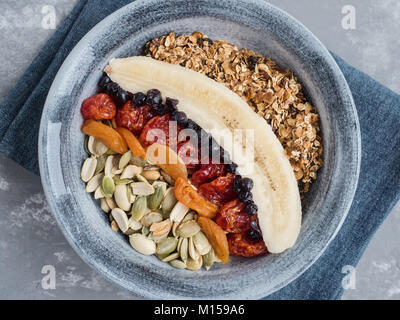Müsli mit Banane, Blaubeeren, getrocknete Aprikosen, carneol Kirsche, Erdnüsse, Kürbiskerne, in einer alten Platte auf einem grauen Tabelle Stockfoto