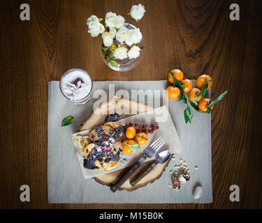 Schöne Teller zum Frühstück auf der stilvoll mit Holz fach Pfannkuchen und Parfait mit Früchten mit Belag auf den Tisch eingerichtet. Bereit zu essen. Close-up Stockfoto