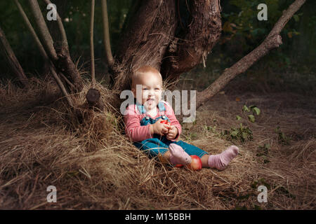 Kleines Mädchen mit Äpfeln sitzt unter einem Baum. Sie ist Lachen Stockfoto