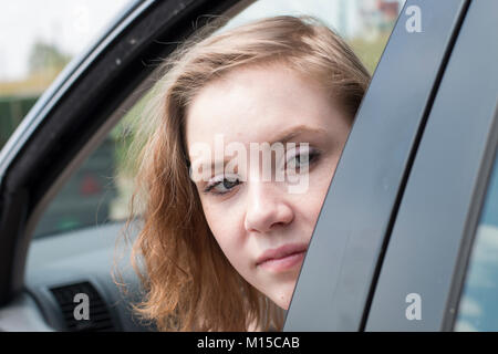 Eine Frau in einem Auto ist Blick aus dem Fenster und sieht zurück, um den Verkehr zu prüfen. Stockfoto