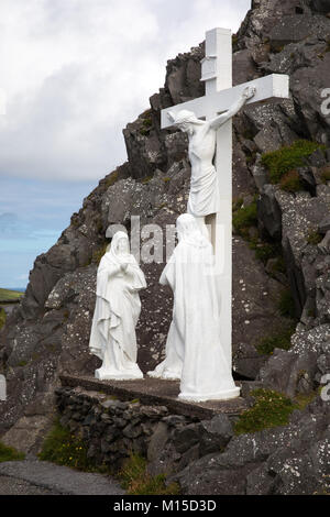Ein weißes Kreuz steht an den dunklen Felsen der Slea Head Drive auf der Halbinsel Dingle, Irland. Stockfoto