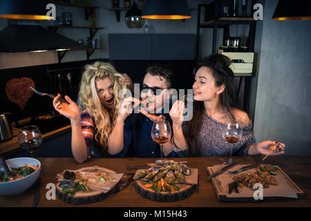 Zwei junge Frauen mit einem Mann lächelt und hat gemeinsam das Abendessen an der Bar. Gruppe von schönen Menschen und isst Essen mit Wein und genießen am Abend Stockfoto