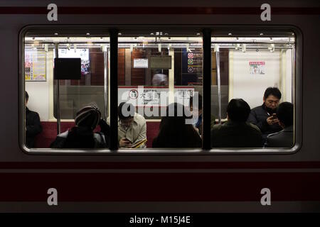 Blick durch das Fenster in das Innere der Marunouchi Linie Zug an Otemachi Station in den frühen Abend mit Fahrgäste, die ihre Telefone. Stockfoto