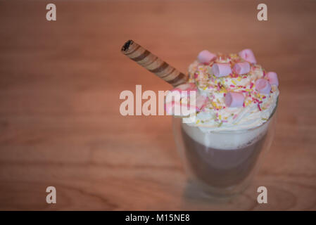 Köstliche heiße Schokolade trinken Drink mit Ansicht des Schlagsahne topping besprüht und rosa Marshmallows auf Holz Tisch Hintergrund Stockfoto