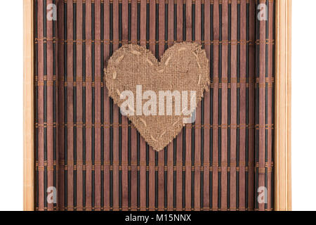 Herz aus Sackleinen liegt auf einem Bambus Matte mit geschwungenen Kanten. Auf weissem Hintergrund. Stockfoto