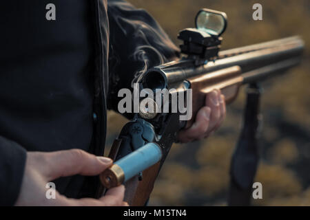 Sport schießen. Hunter nachladen Patrone in das Feld ein. Rauch aus den Stämmen von glattem Jagdwaffe nach dem Feuern. Stockfoto