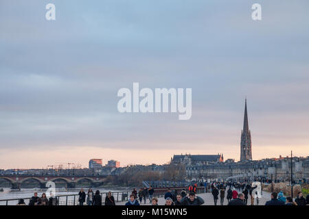 BORDEAUX, Frankreich - 24. Dezember 2017: Garonne Quays (Quais de la Garonne) in der Dämmerung mit einer Menge vorbei. Saint Michel Basilika können in Backgr gesehen werden Stockfoto