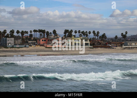 Mehrfarbige Beach cottages säumen die Ufer im Imperial Beach, Kalifornien, vom Pier gesehen. Einstellung der Wellen brechen am Strand, die Wolken im Himmel Stockfoto