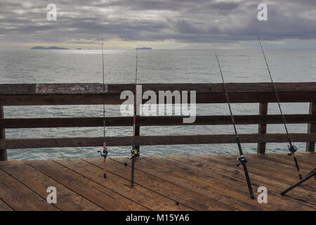 Vier Fischereipfosten ruht auf dem Geländer der Imperial Beach Pier in Kalifornien am bewölkten Tag, den Pazifischen Ozean und Coronado Inseln im Hintergrund Stockfoto