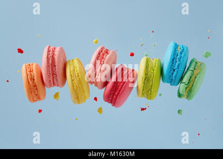 Verschiedene Arten von Makronen in Bewegung fallen auf blauem Hintergrund. Süße und bunte französische Macarons fallen oder fliegen in Bewegung. Stockfoto