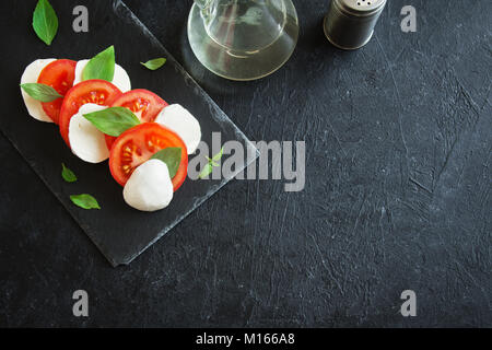 Traditionelle italienische Caprese Salat - in Scheiben geschnittenen Tomaten, Mozzarella und Basilikum auf dunklem Stein, Ansicht von oben, Copyspace. Caprese Salat, Italienisch Stockfoto