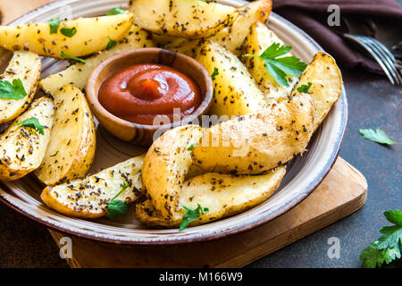 Gebackene Kartoffelecken mit Käse und Kräutern und Tomatensauce auf schwarzem Hintergrund - hausgemachte Bio-gemüsegarten vegan vegetarische Potato Wedges Snack essen. Stockfoto