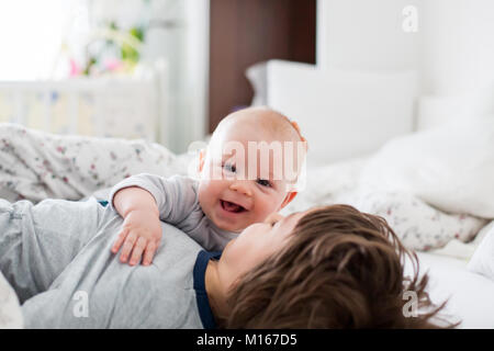 Zwei Kinder, Baby und sein älterer Bruder im Bett am Morgen, gemeinsam spielen, lachen und eine gute Zeit, die gemeinsame Nutzung von speziellen Moment, Kleben Stockfoto