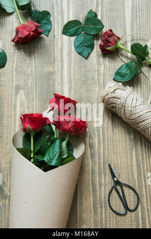 Florist eine rote Rosen Blumenstrauß, Umwickeln mit Kraftpapier auf einem Holztisch. Blick von oben. Im rustikalen Stil. Stockfoto