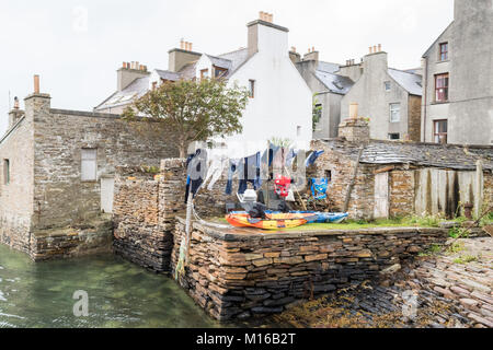 Kajaks und Neoprenanzüge trocknen auf der Wäscheleine im Garten direkt am Meer in Stromness, Orkney, Schottland, Großbritannien Stockfoto