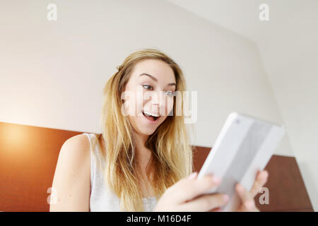 Crazy glückliche junge Frau smilling mit Tablet am weißen Bett Stockfoto