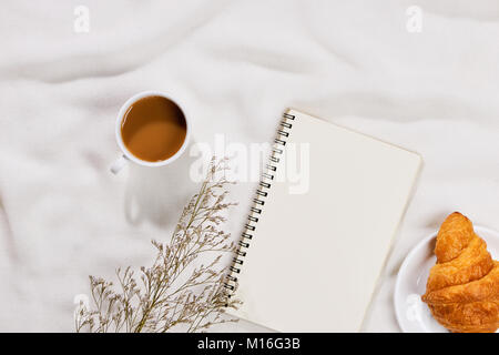 Gemütlich und lecker Frühstück mit Kaffee Tasse und ein Croissant mit Papier. Stockfoto