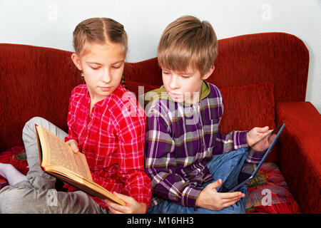 Das Mädchen erweist sich sein Bruder den Vorteil der grundlegenden Bücher vor dem Lesen von einem elektronischen Tablet Stockfoto