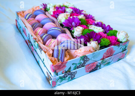 Französische Makronen Kuchen. Violett und Rosa Makronen in einer Box mit Blumen auf dem Bett. Stockfoto