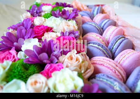 Französische Makronen Kuchen. Violett und Rosa Makronen in einer Box mit Blumen auf dem Bett. Stockfoto