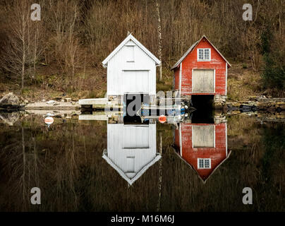 Nedstrand in Norwegen - Januar 10, 2018: Zwei alte Hölzerne Bootshäuser in der Stille Ozean wider. Die norwegische Westküste, Norwegen Stockfoto