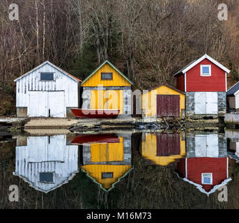 Nedstrand in Norwegen - Januar 10, 2018: Vier alte Hölzerne Bootshäuser in der Stille Ozean wider. Die norwegische Westküste, Norwegen Stockfoto