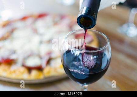 Besonderen Anlass zum Feiern - Rotwein wird aus Flasche in Glas in Restaurant oder Cafe gegossen, im Hintergrund gibt es Silhouette von Pizza. Stockfoto