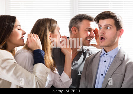 Business Kollege Whispering geheimen Klatsch zu einem entsetzten Mann mit weit geöffneten Mund geschockt Stockfoto