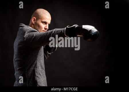 Ein glatzköpfiger Mann Manager in einem weißen Hemd, grauen Anzug, Boxhandschuhe Boxen auf einem schwarzen Hintergrund isoliert Stockfoto