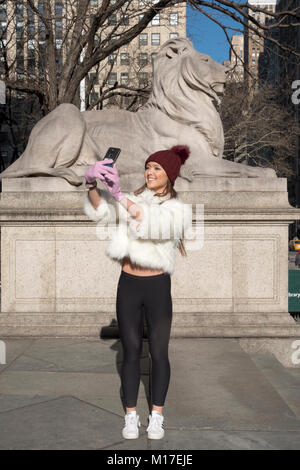 Eine sehr hübsche junge Dame nimmt eine selfie vor der Statue des Löwen vor der wichtigste Zweig der New York Public Library. Stockfoto