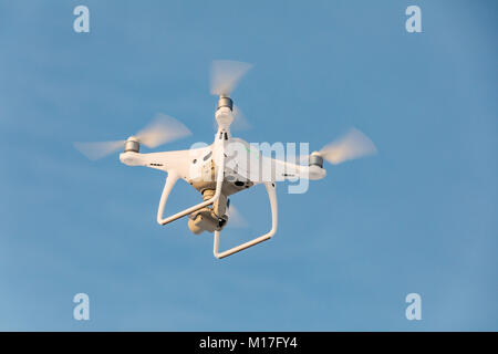 Fliegen weiß drone Phantom auf den blauen Himmel. Landung eines summten Hand mit drehenden Propellern Stockfoto