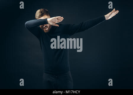 Anonyme Mann in Schwarz stylisches Outfit für Gesicht mit den Händen tanzen auf schwarzem Hintergrund. Stockfoto