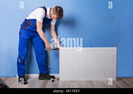 Junge männliche Klempner in Uniform Einbau des Kühlers mit einem Schraubenschlüssel Stockfoto